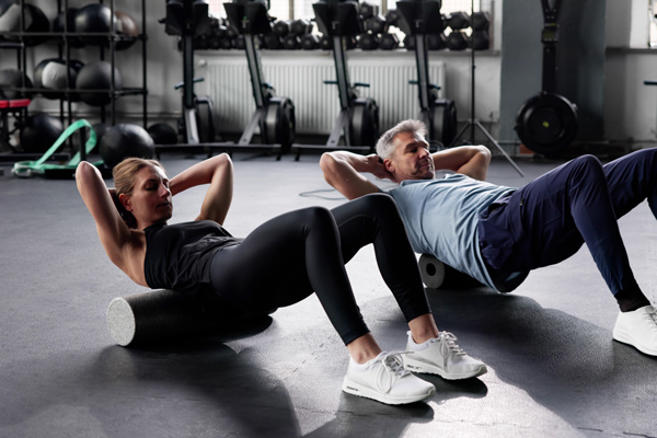 two fitness enthusiasts performing ab exercises on foam rollers in a gym setting focusing on core strength and endurance improving health and wellness eight workouts a week