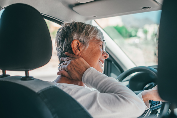 smiling older woman driving car with hand on neck experiencing discomfort while enjoying 10 tips for safe driving