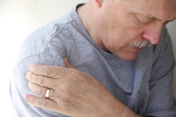 senior man with gray shirt holding shoulder possibly in pain experiencing discomfort aged 5 years or more