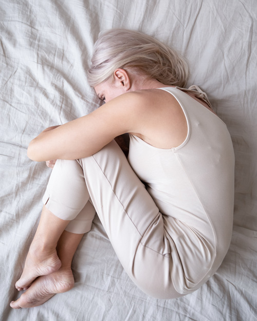woman curled up in a fetal position on a bed with soft bedding representing calmness and comfort in a peaceful setting 2 moments of tranquility 2 signs of self care