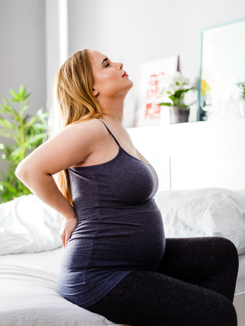 pregnant woman sitting on bed experiencing back pain in bright room wellness and comfort during pregnancy 2nd trimester